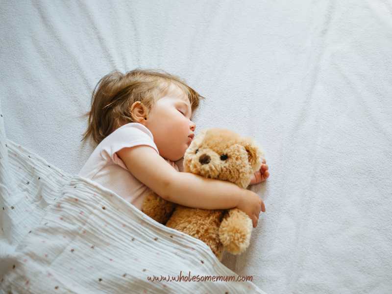 baby-girl-sleeping-on-white-bed-while-cuddling-with-a-teddy-bear