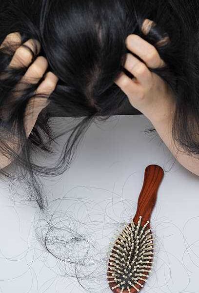 A woman holding her hair and feeling downcast because hair is shedding due to postpartum hair lost.