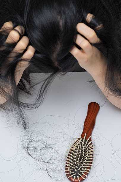 A woman holding her hair and feeling downcast because hair is shedding due to postpartum hair lost.